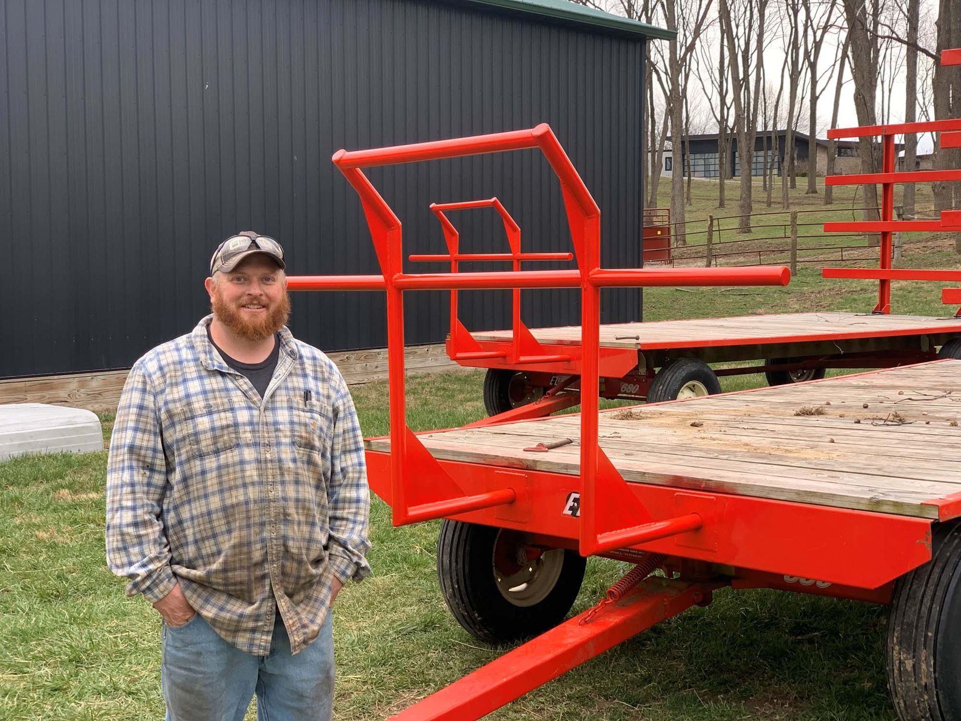 A man in a plaid shirt is standing in front of a red trailer.