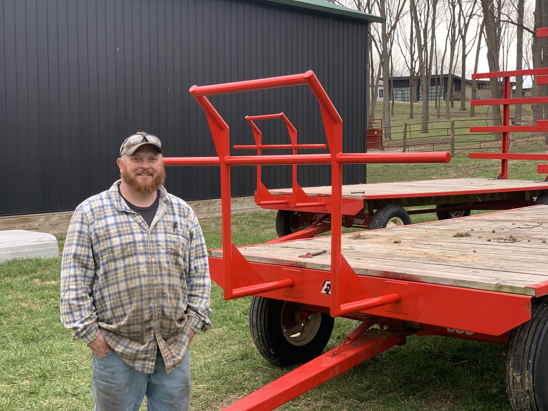 A man in a plaid shirt is standing next to a red trailer.