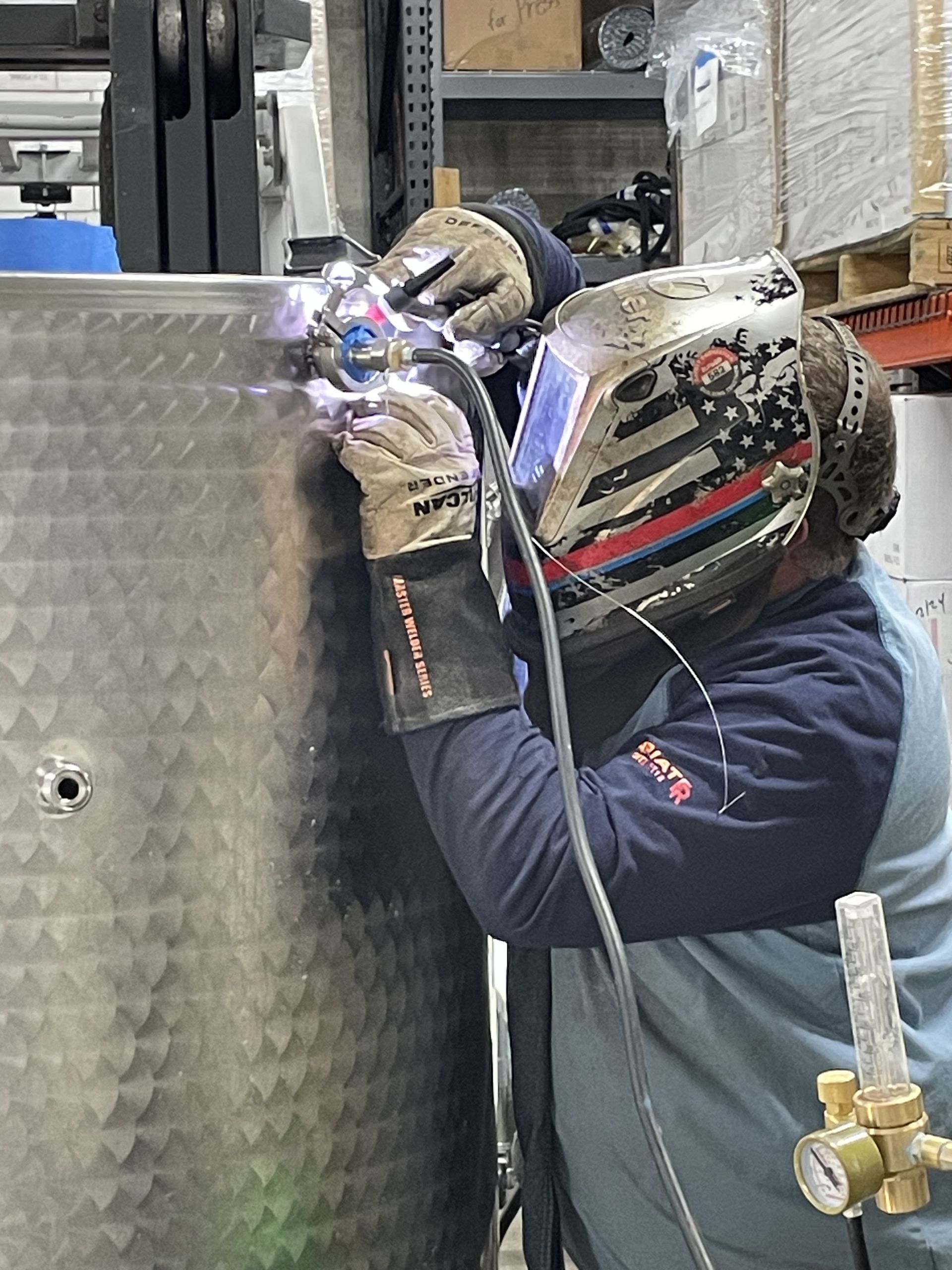 A man wearing a welding helmet is welding a metal object.
