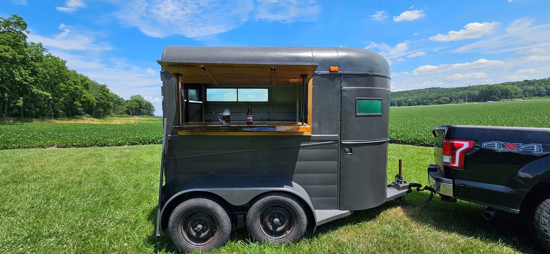 A horse trailer is parked in a grassy field next to a truck.