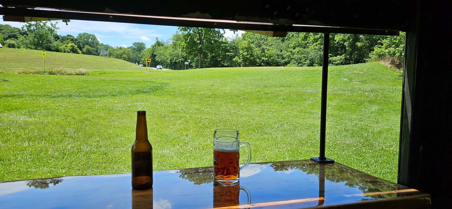 A bottle of beer and a glass of beer are on a table in front of a field.