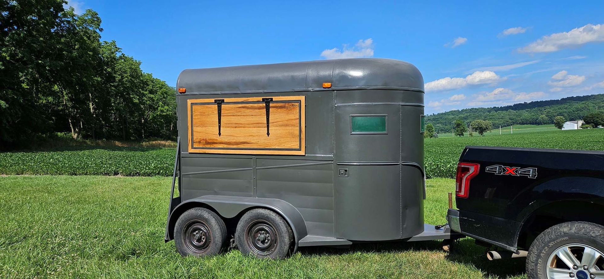 A horse trailer is being towed by a truck in a grassy field.