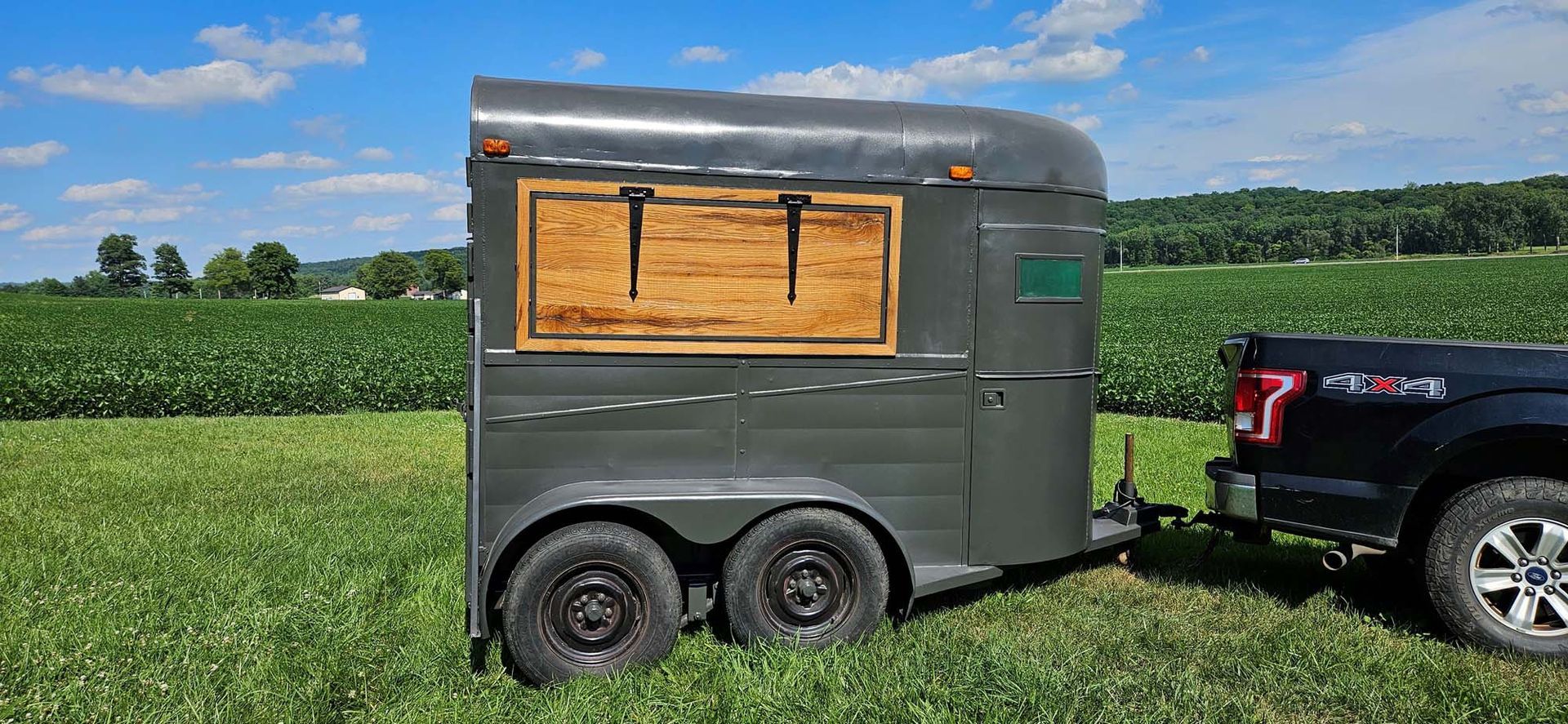 A horse trailer is being towed by a truck in a field.