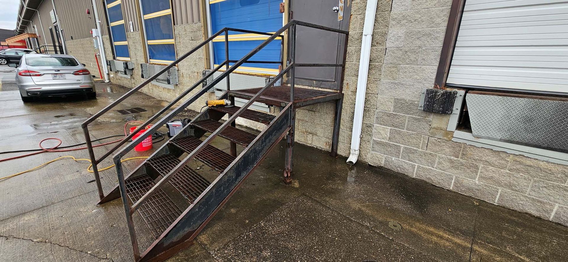 A car is parked in front of a building with stairs leading up to it.