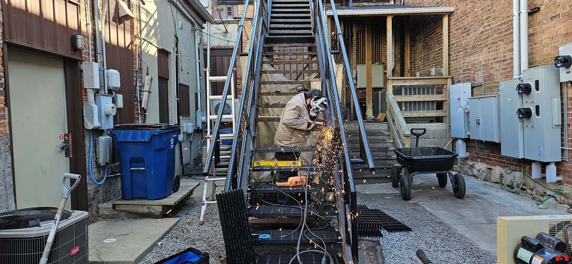 A man is welding a metal railing in a backyard.