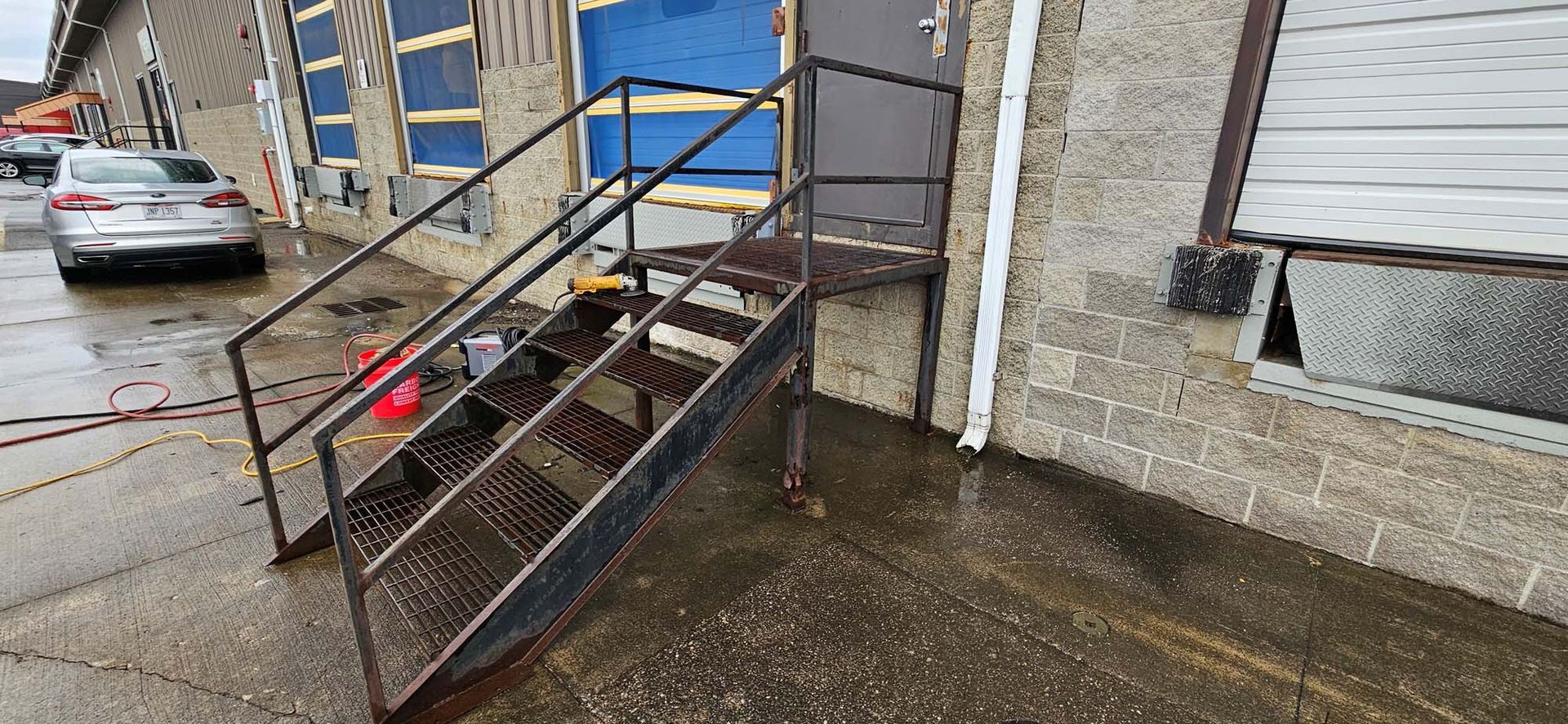 A car is parked in front of a building with stairs leading up to it.