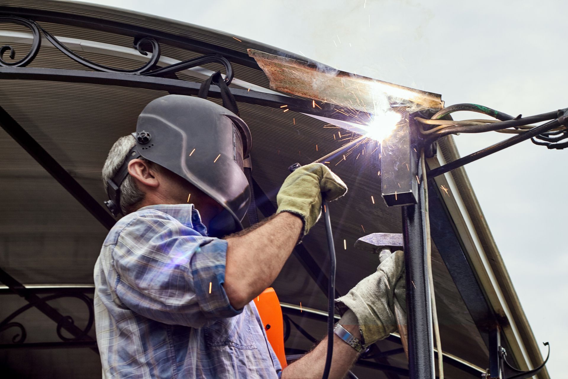 A man wearing a welding mask is welding a metal structure.