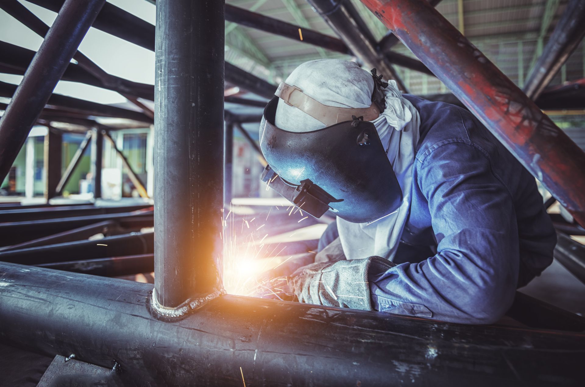A man is welding a metal pipe in a factory.