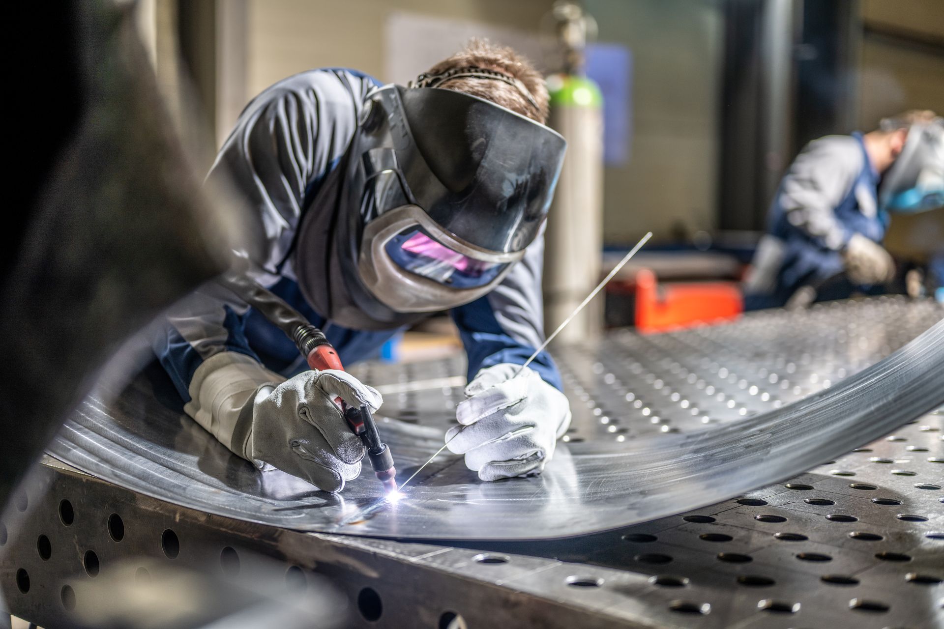 A man is welding a piece of metal in a factory.