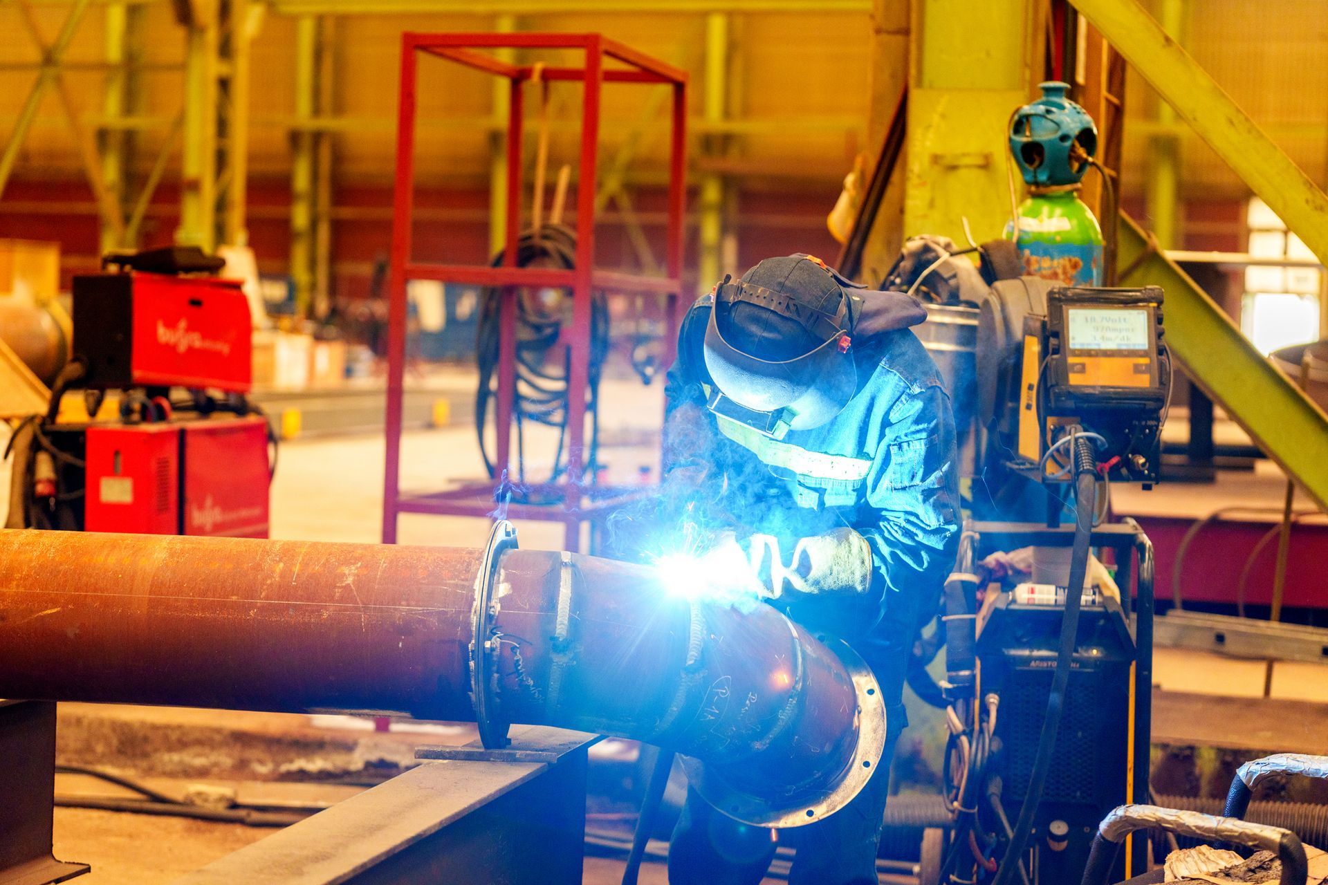 A man is welding a pipe in a factory.