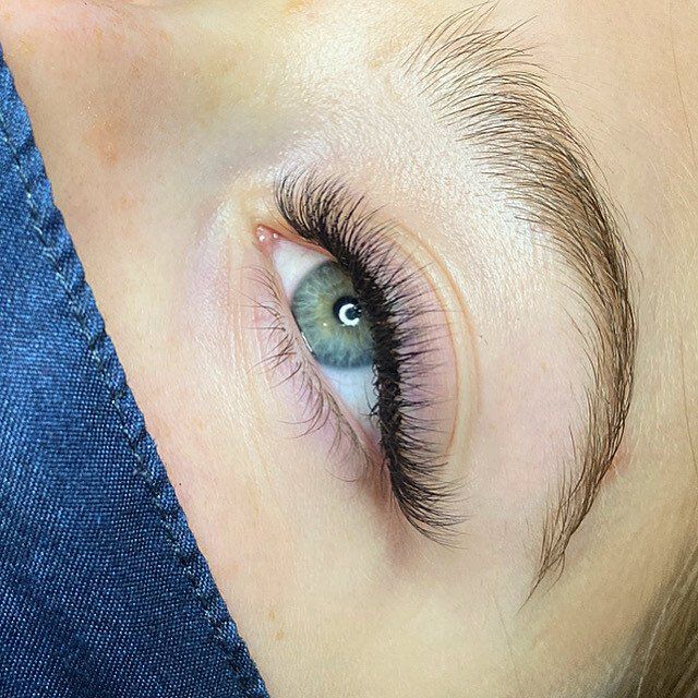 Close-up of a light-skinned eye with long, dark lash extensions. The eye is blue-green, and the brow is neatly shaped.