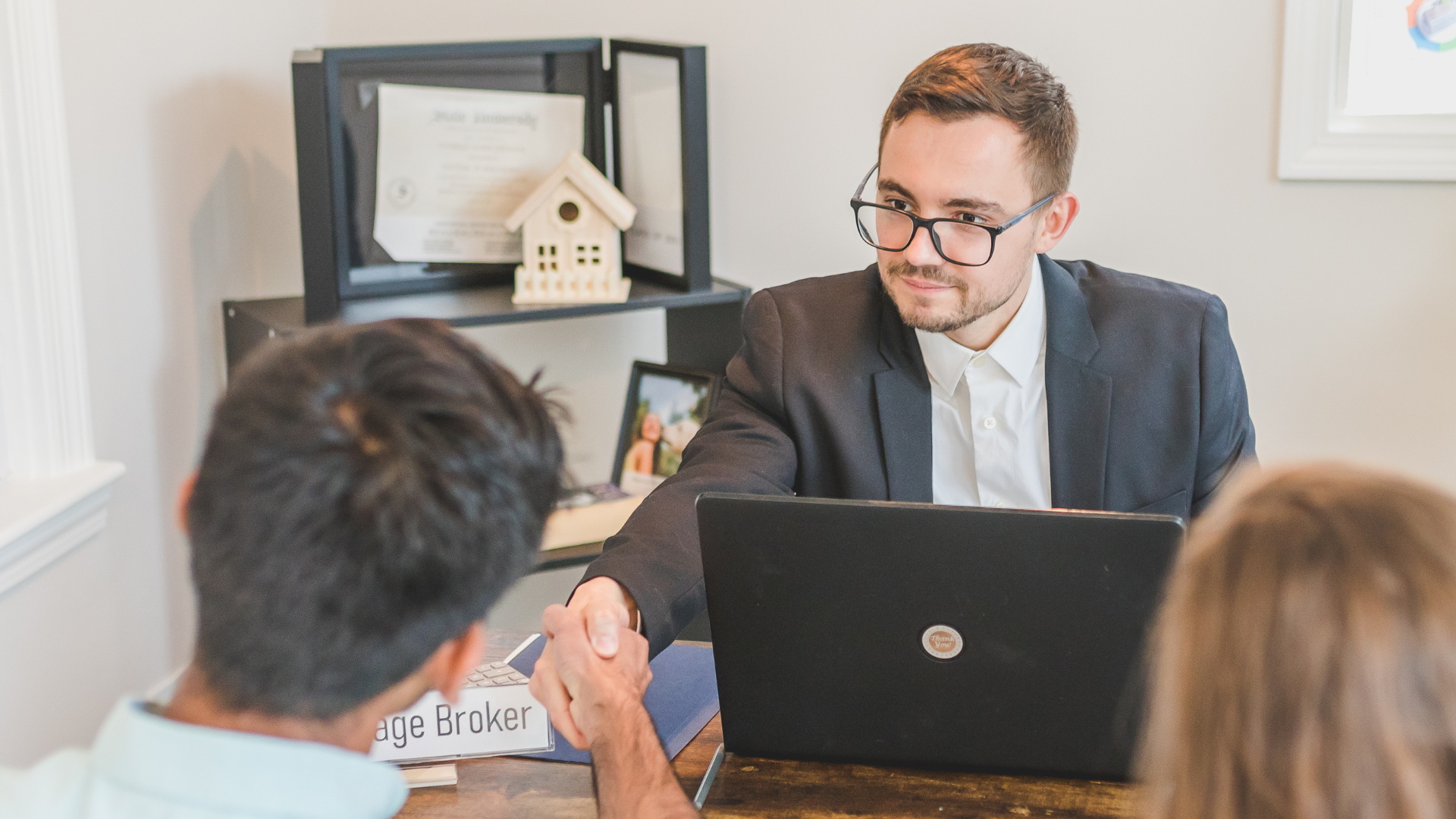 A man in a suit is shaking hands with a man in front of a laptop computer.