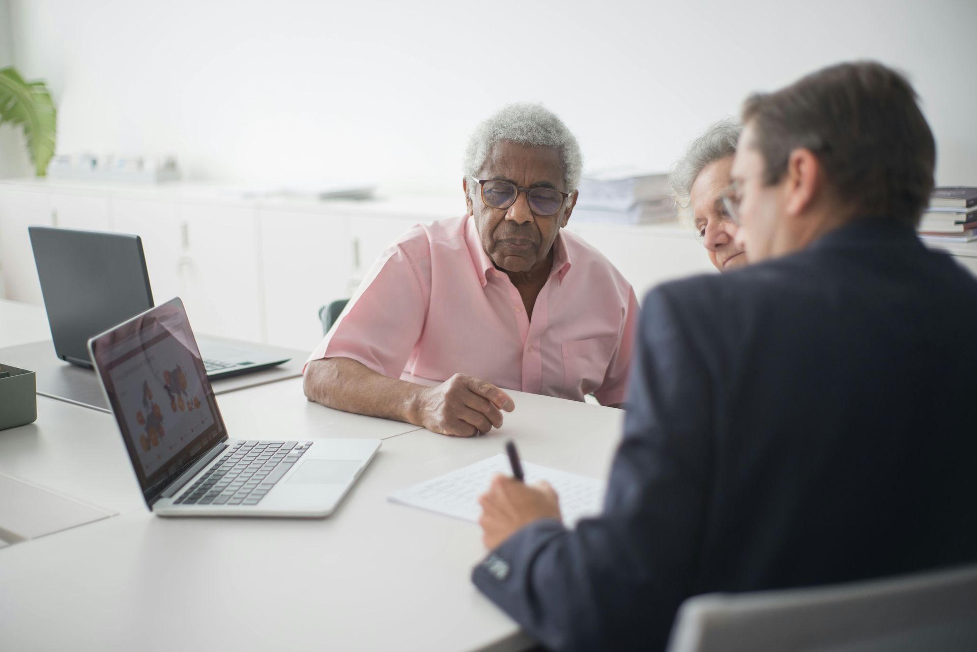 A man is sitting at a table with a laptop and shaking hands with a man.