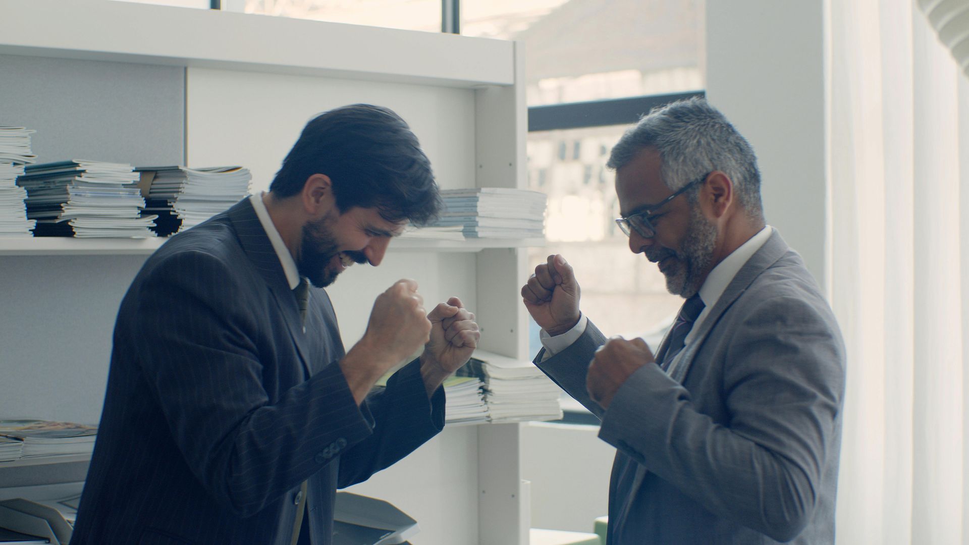 A man is sitting at a table with a laptop and shaking hands with a man.