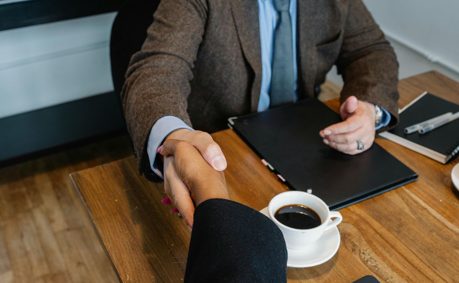 A man is sitting at a table with a laptop and shaking hands with a man.