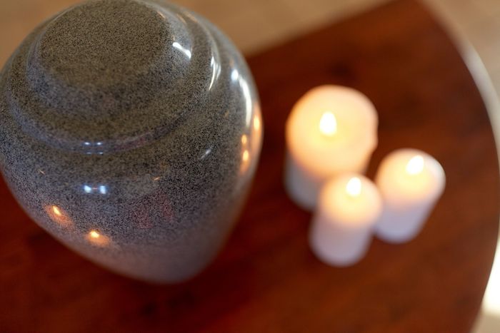 Un'urna grigia e lucida accanto a tre candele bianche accese su una superficie di legno scuro.