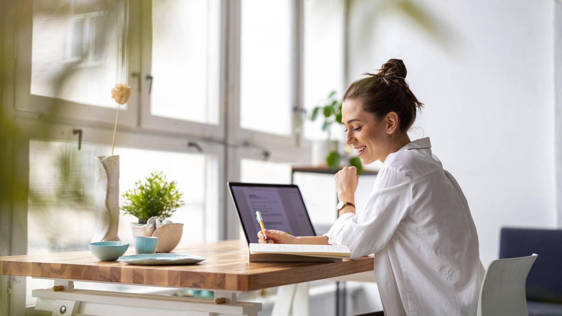 A woman working at her contemporary home office desk facing windows without Hunter Douglas window tr