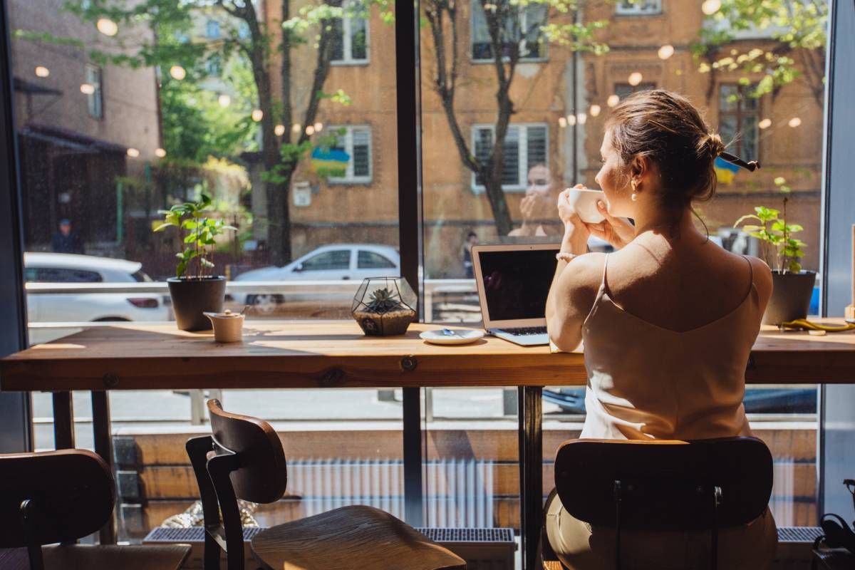 Woman with a laptop, drinking coffee and sitting by a large window at a coffee shop near Houston, TX