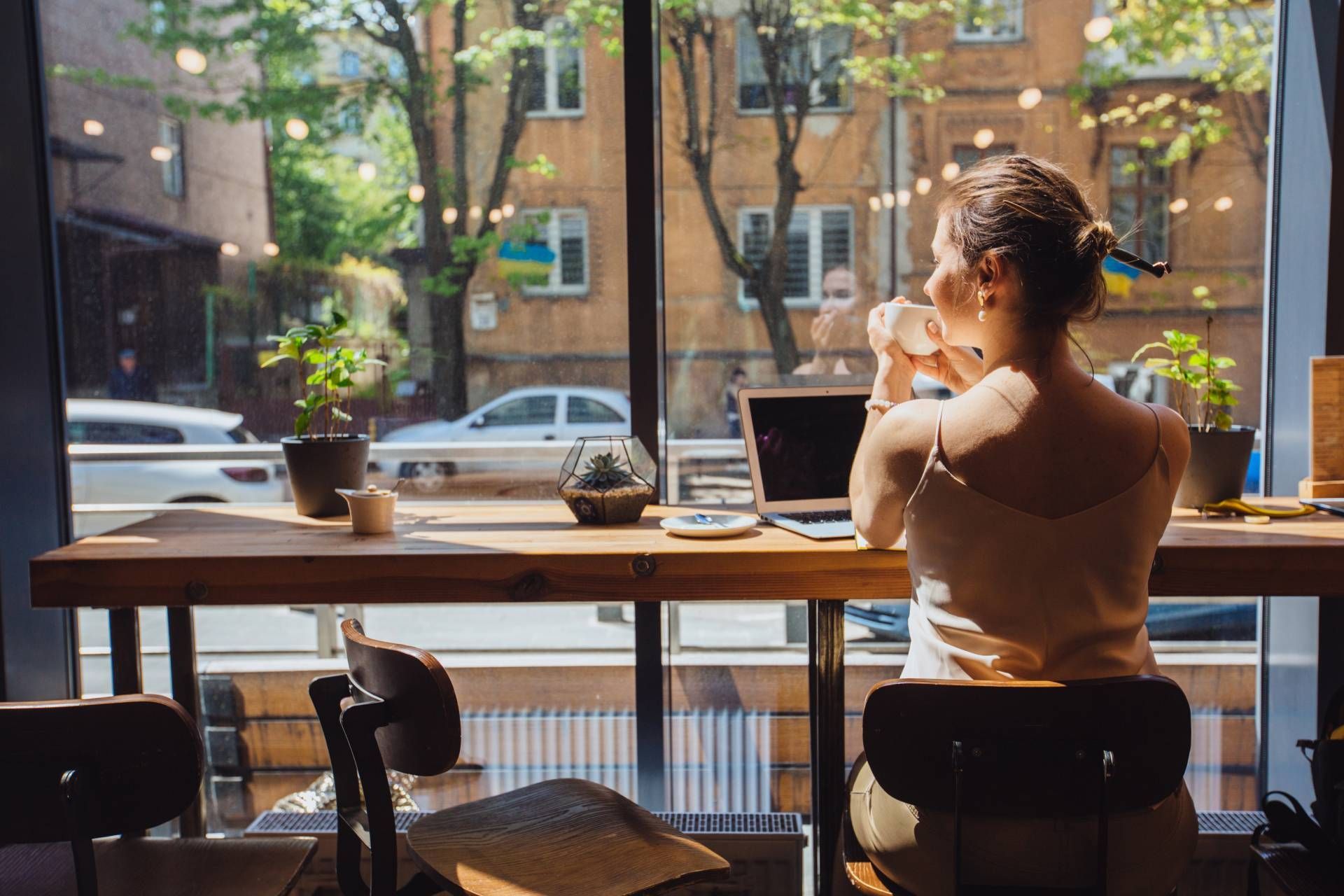 Woman with a laptop, drinking coffee and sitting by a large window at a coffee shop near Houston, TX