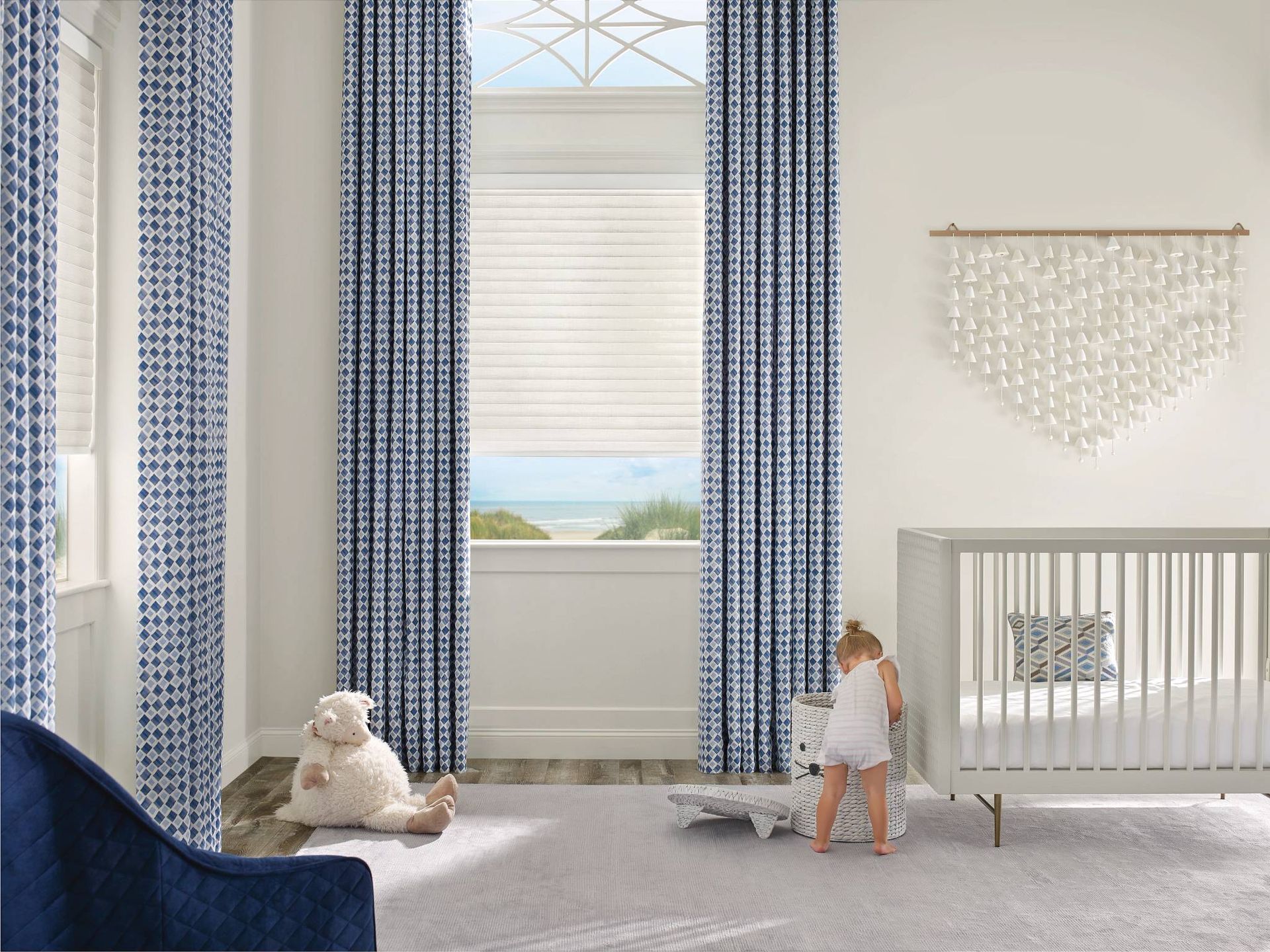 Sonnette® Roller Shades on tall windows in a white and blue nursery, layered with patterned drapes  