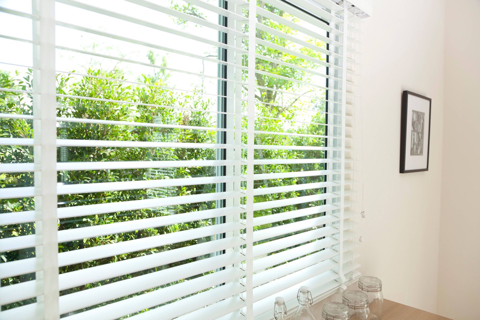 Residential home with a large window, dressed with white blinds, overlooking a greenery-filled backyard near Houston, TX
