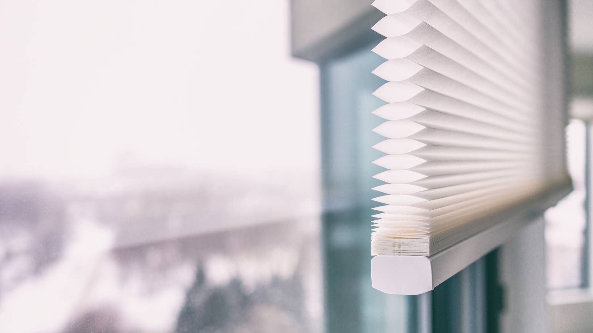 A pleated white cordless window blind on a large window overlooking an outside balcony at Window Mag