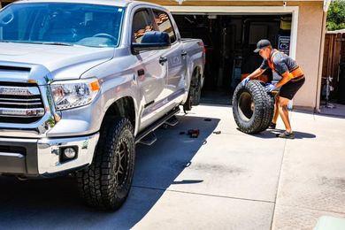 A man is changing a tire on a silver truck