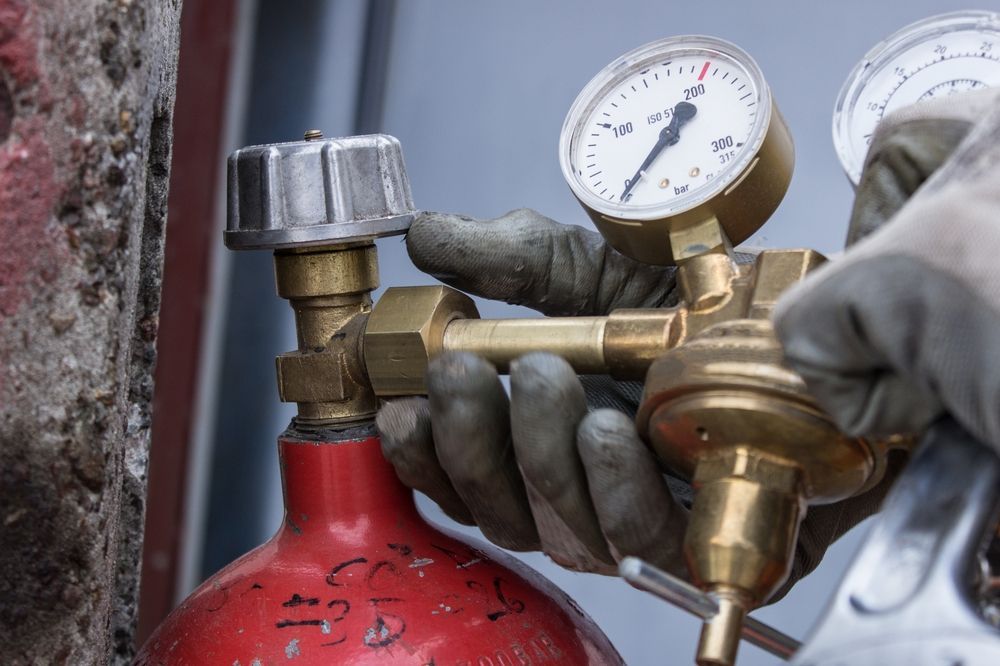 A Gloved Hand Adjusts a Brass Pressure Regulator — Port Macquarie Plumbing In Lake Cathie, NSW