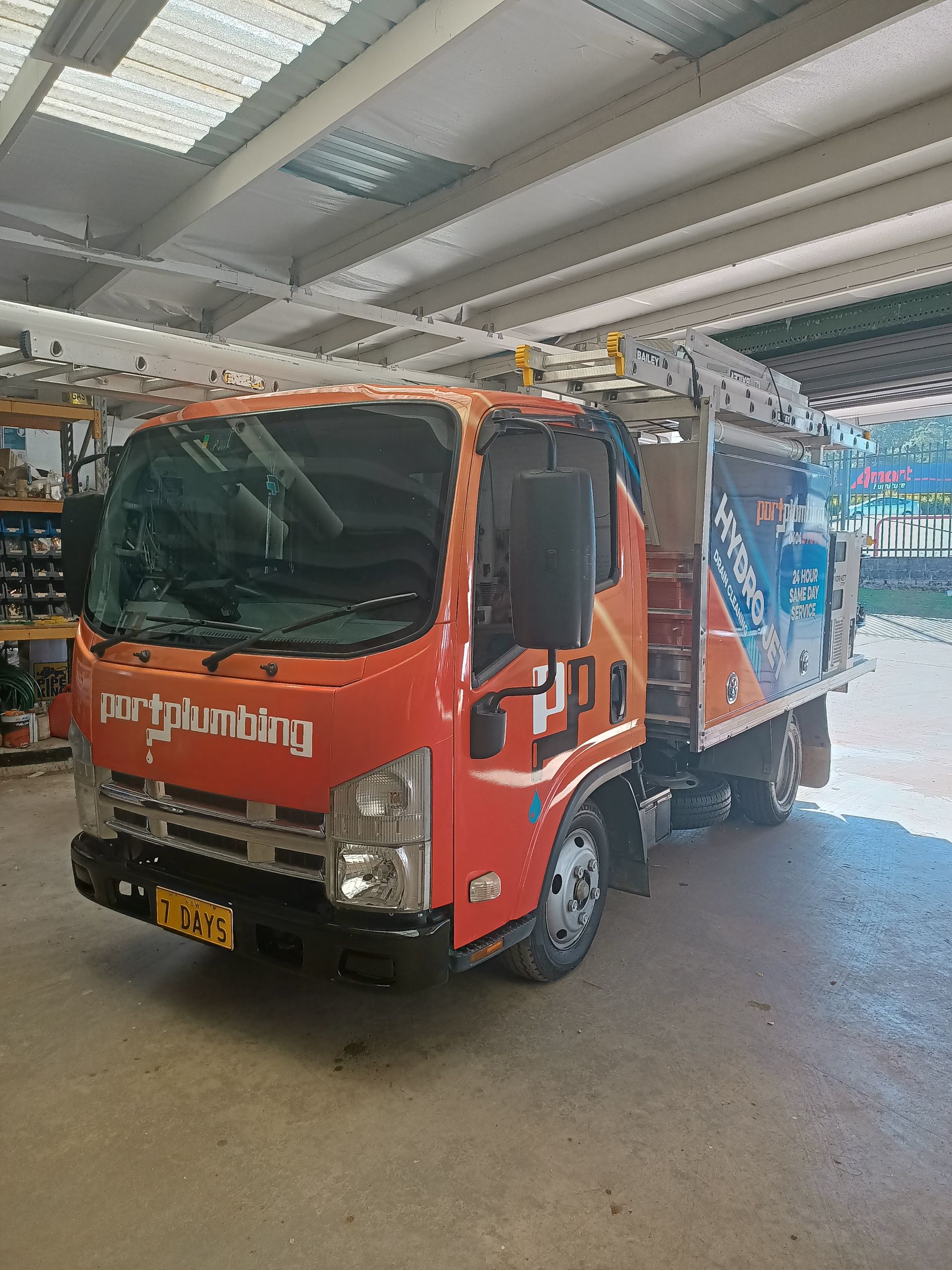 An Orange and Blue Utility Service Truck Parked Inside a Bright, Industrial Workshop Garage — Port Macquarie Plumbing In Port Macquarie, NSW