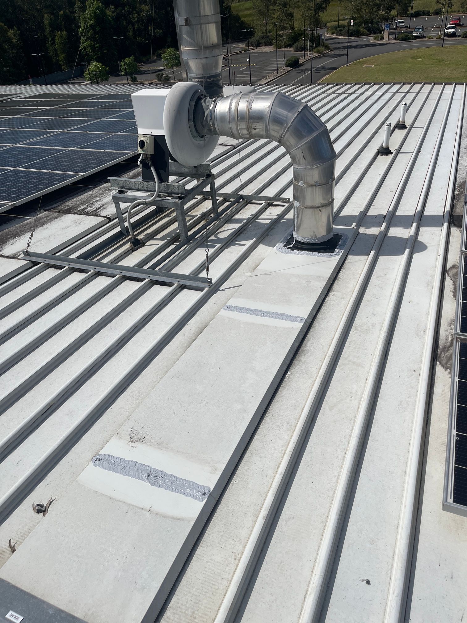 Rooftop Vent Pipe and HVAC Equipment on A White Corrugated Roof Near Solar Panels — Port Macquarie Plumbing In Port Macquarie, NSW