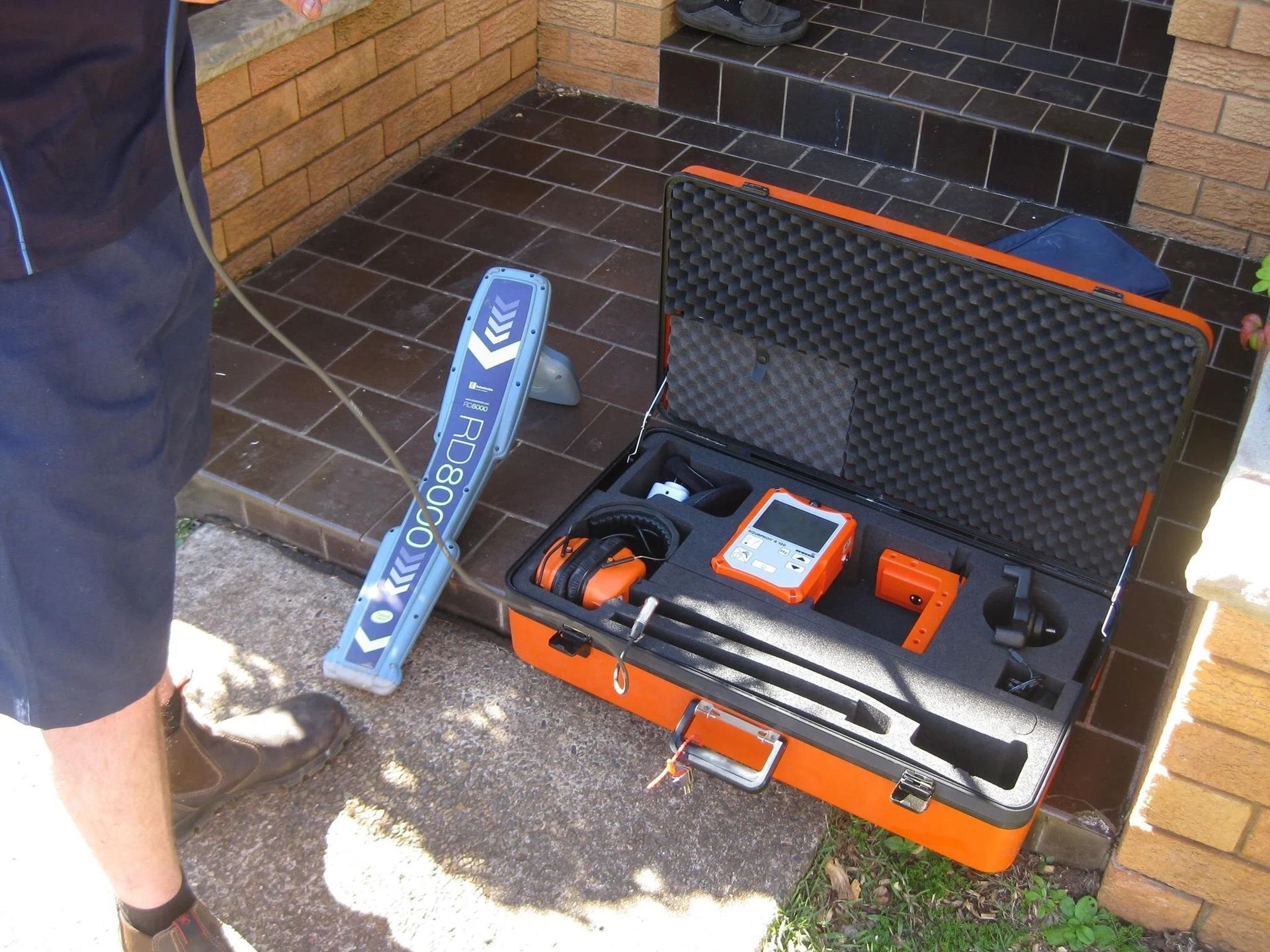Open Orange Tool Case with Handheld Equipment on A Brick Porch — Port Macquarie Plumbing In Port Macquarie, NSW