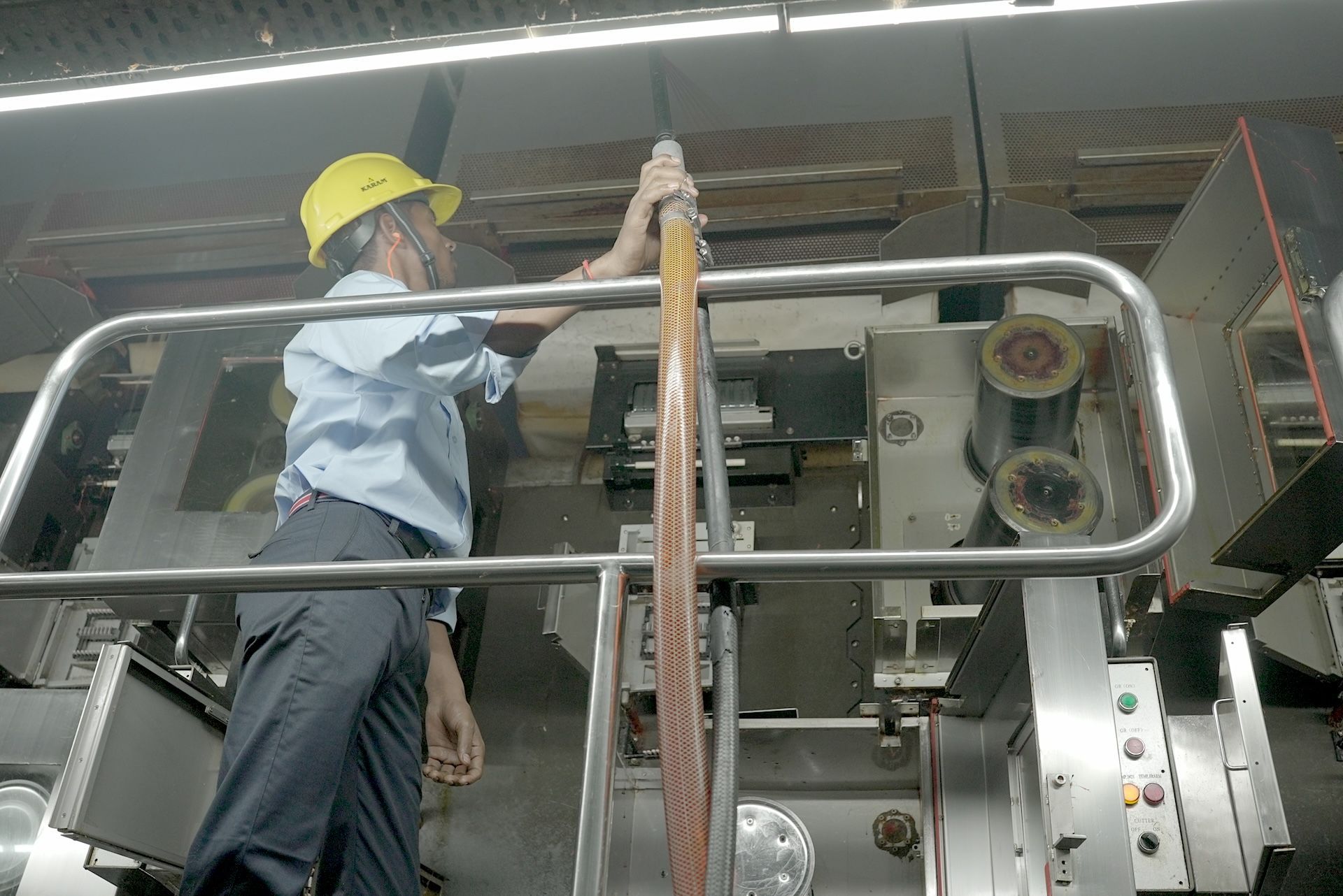 A man wearing a yellow hard hat is working on a machine.