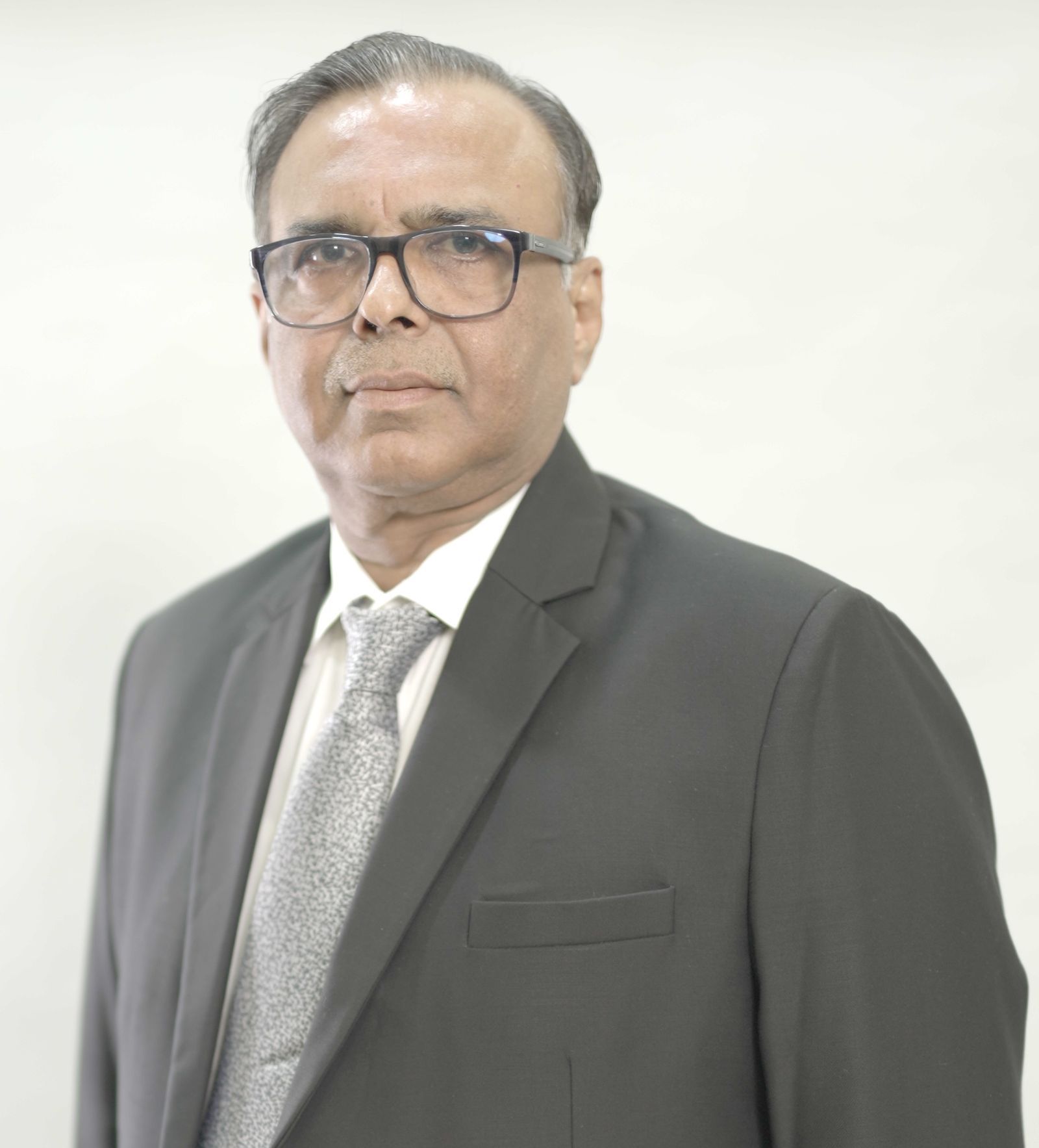 A man in a suit and tie is standing in front of a white wall.