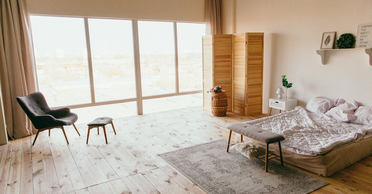 A bedroom with a bed , chair , rug and large windows.