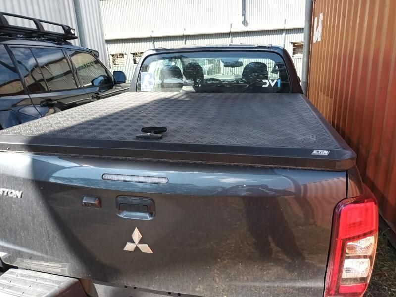 A Black Mitsubishi Truck With a Black Bed Cover is Parked in Front of a Building — South West 4WD Wreckers In Harristown, QLD