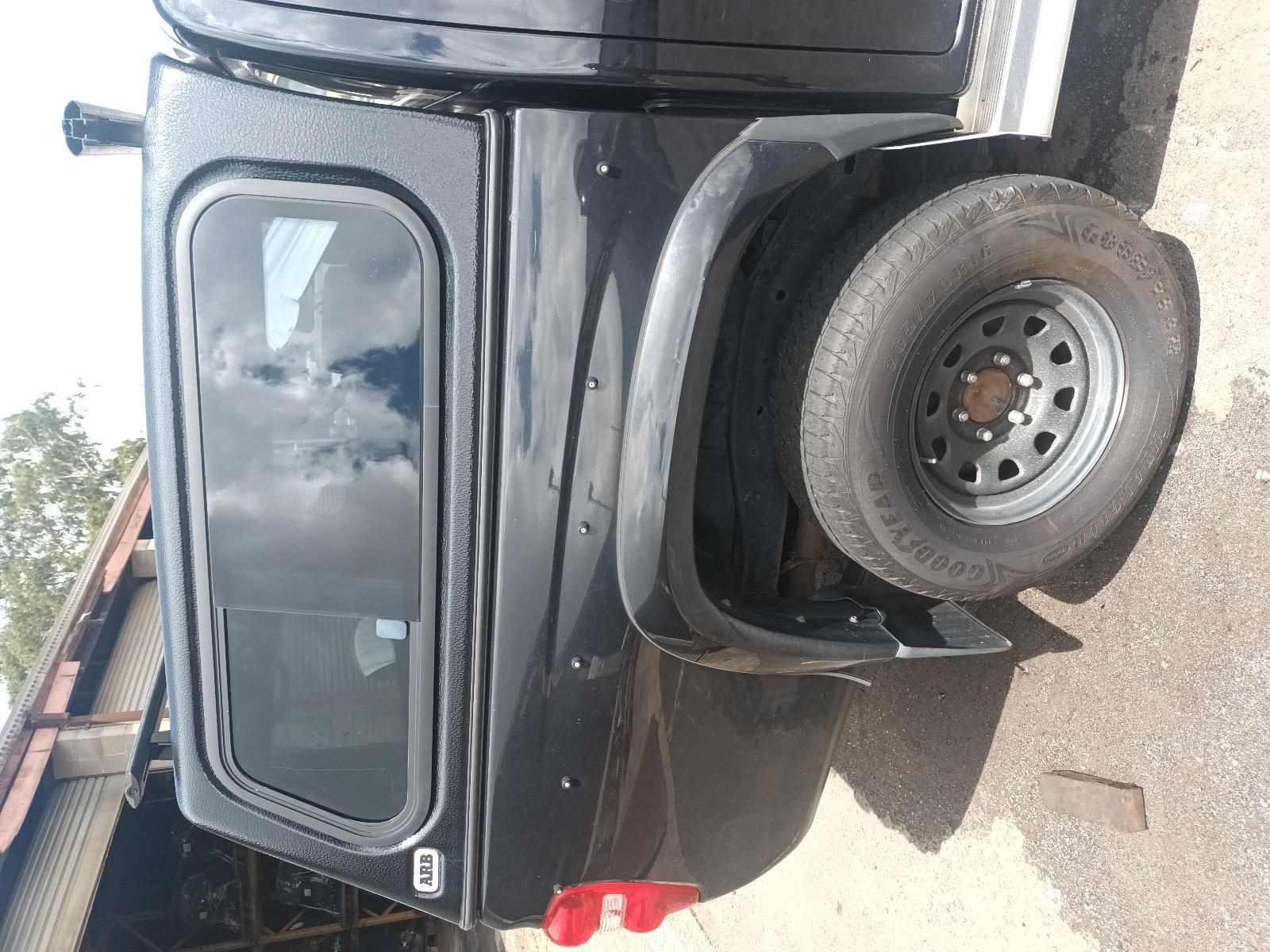 A Black Truck with a Canopy and a Tire is Parked on the Side of the Road — South West 4WD Wreckers In Brisbane, QLD