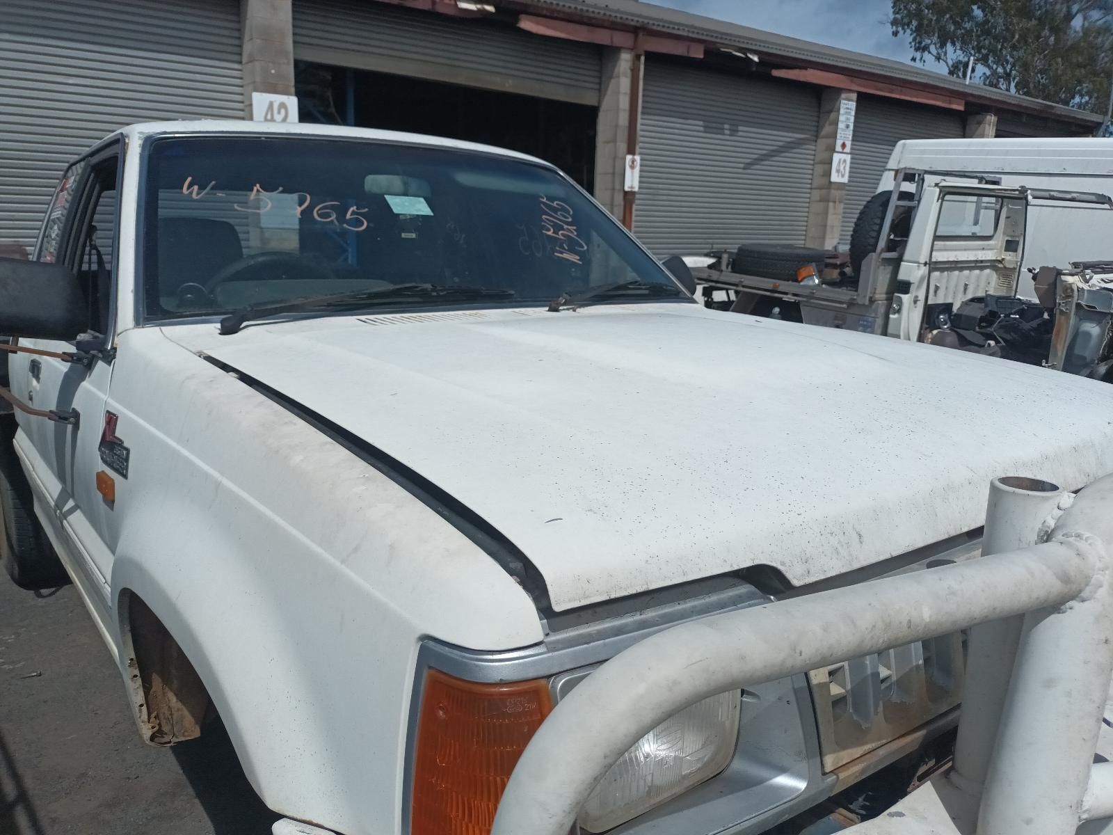 A White Truck with a Broken Hood is Parked in Front of a Garage — South West 4WD Wreckers In Brisbane, QLD