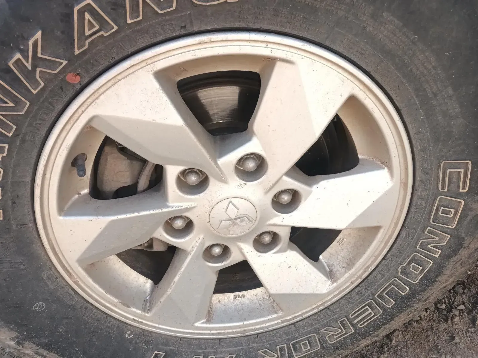 Silver Alloy Wheel With a Mitsubishi Emblem on a Dirty Tyre — South West 4WD Wreckers In Brisbane, QLD