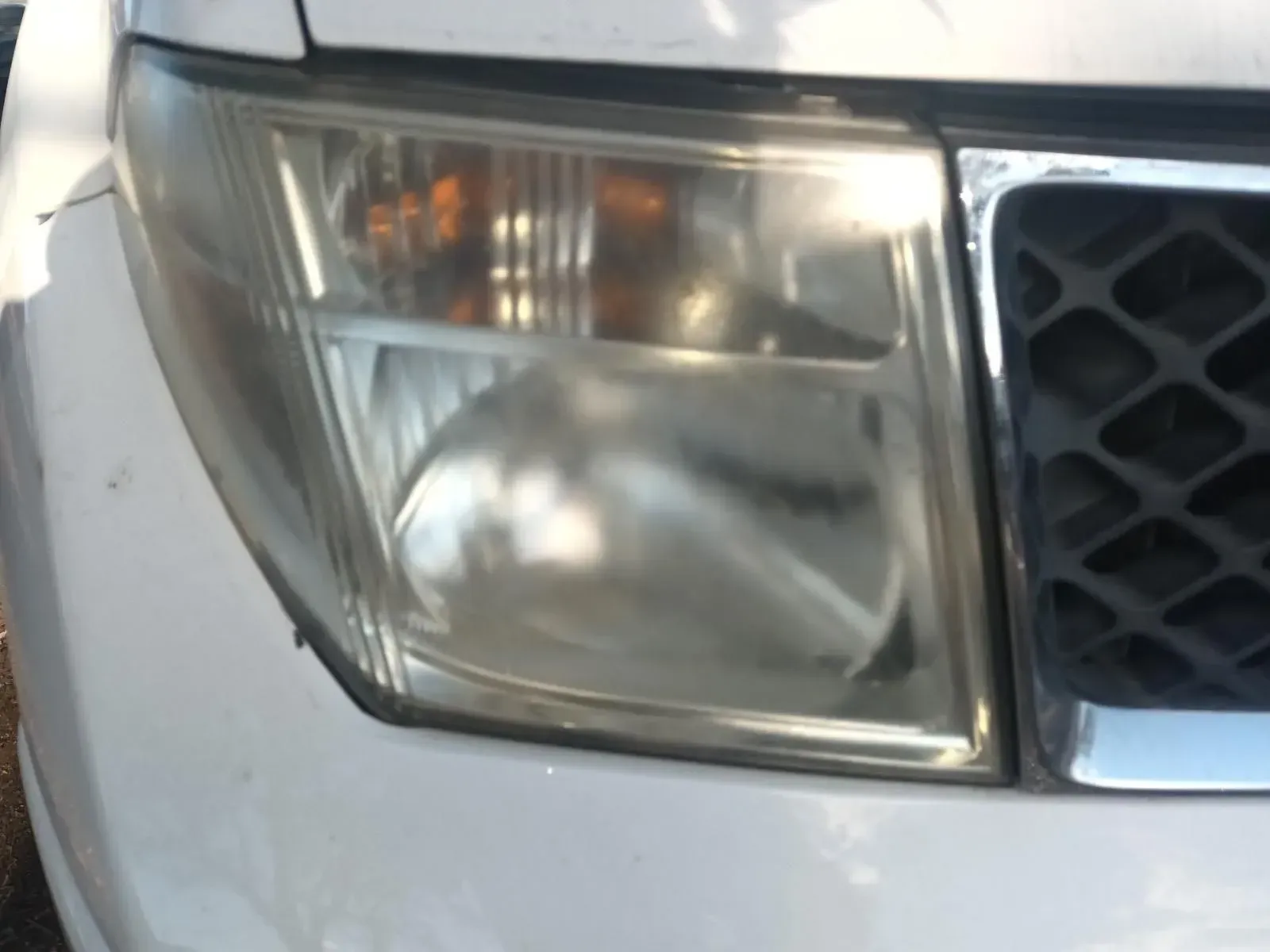 Close-up of a Cloudy Headlight on a White Car Next to a Black Grill — South West 4WD Wreckers In Brisbane, QLD