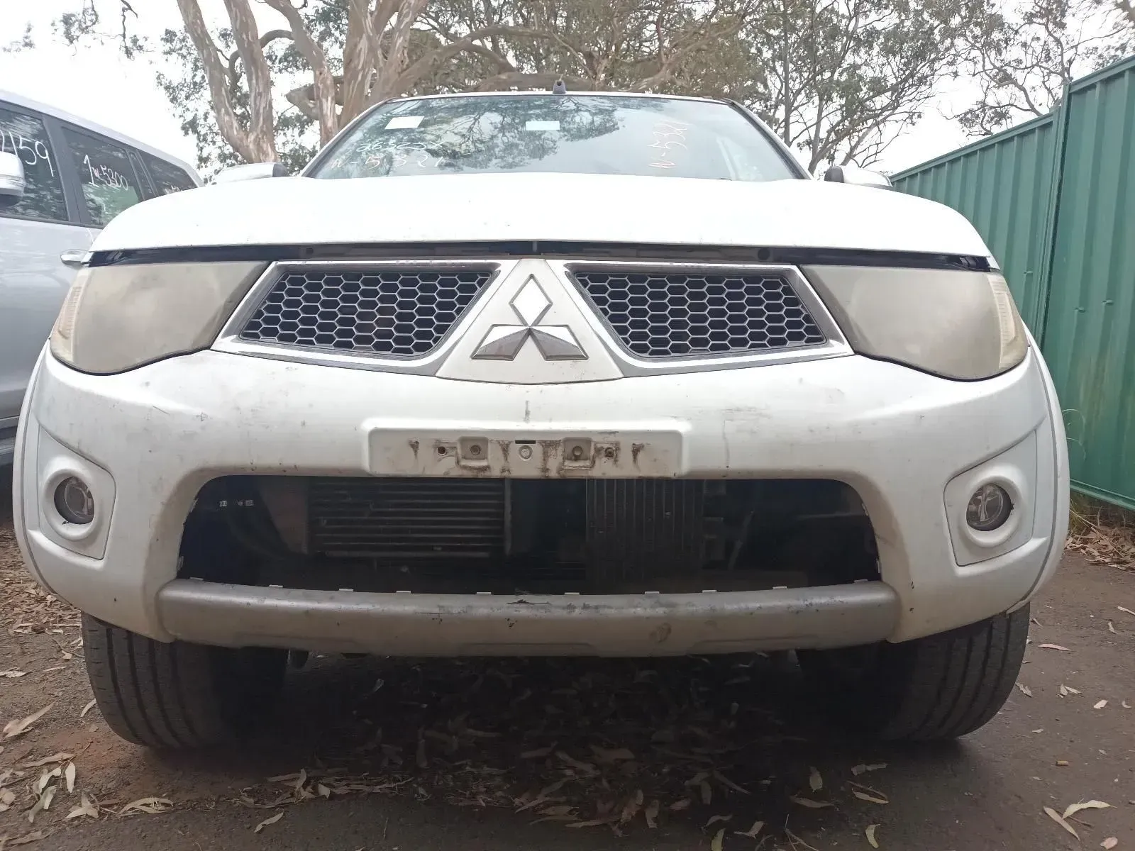 White Mitsubishi Triton Truck, Front View, Missing Headlights, in a Yard Setting — South West 4WD Wreckers In Brisbane, QLD