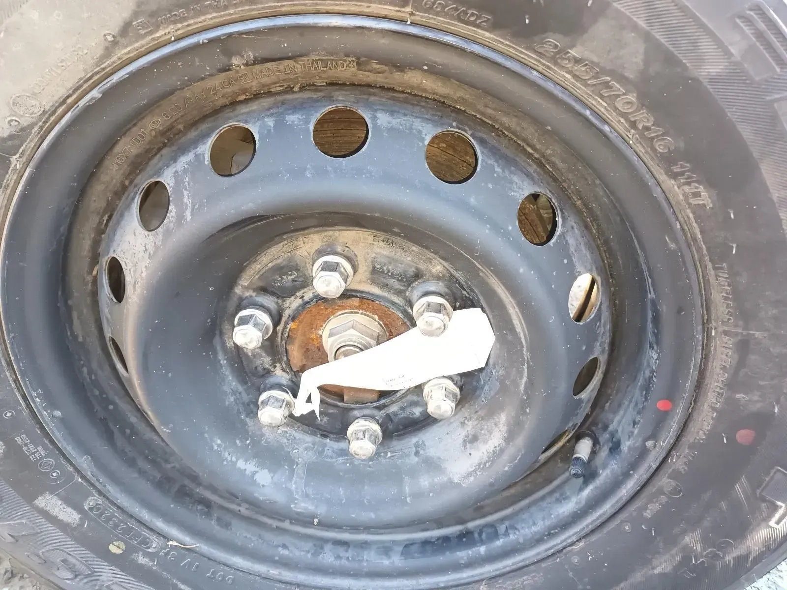 Black Car Wheel With Hubcaps, Dirty Tyre, Lug Nuts, and Paper Attached — South West 4WD Wreckers In Brisbane, QLD
