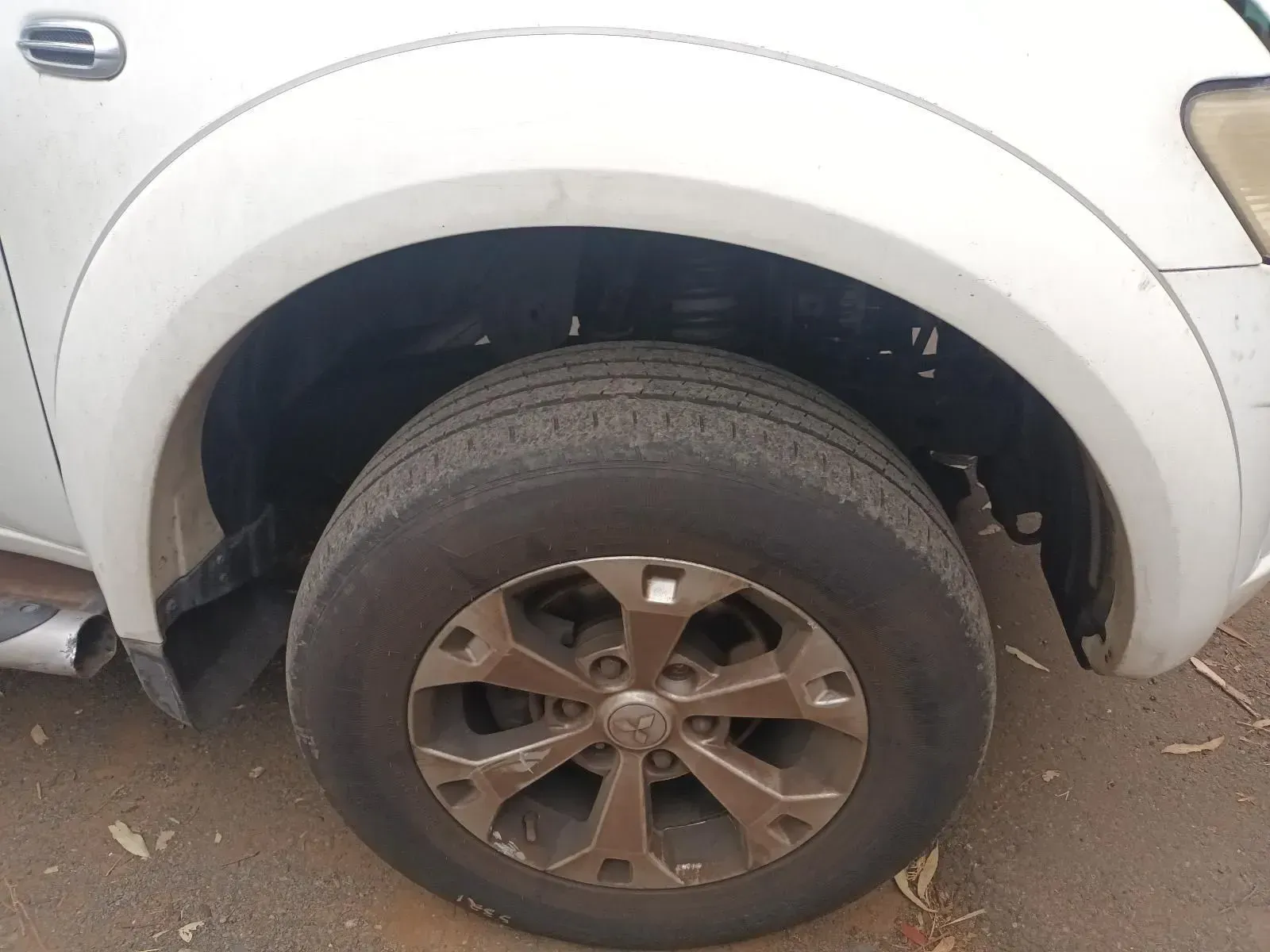 White Car's Front Tyre and Wheel. Dusty, Worn Tyre With a Grey Rim — South West 4WD Wreckers In Brisbane, QLD