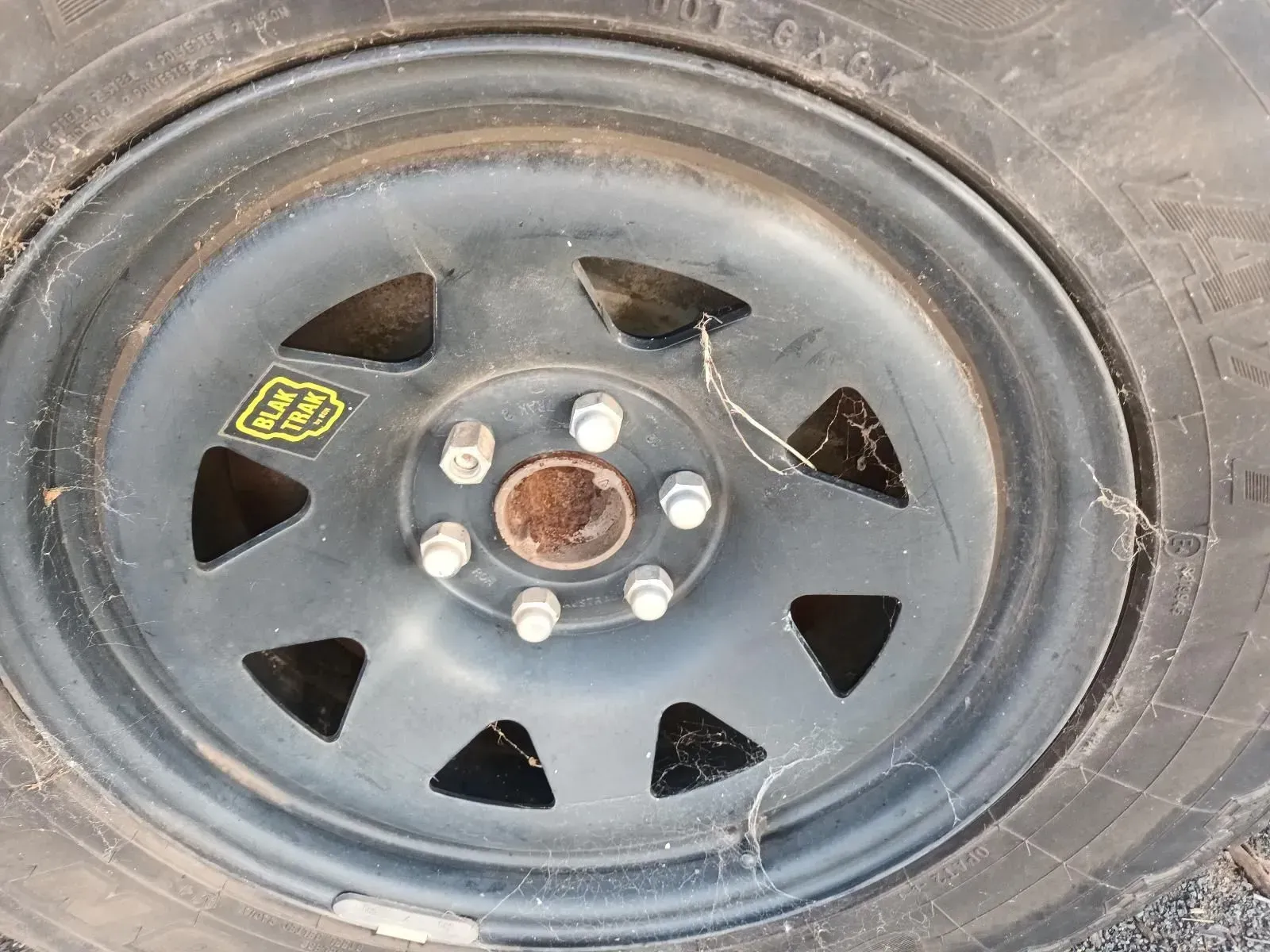 Black Car Tyre With Six Bolts, Showing a Rusty Center Cap and Web Debris — South West 4WD Wreckers In Brisbane, QLD