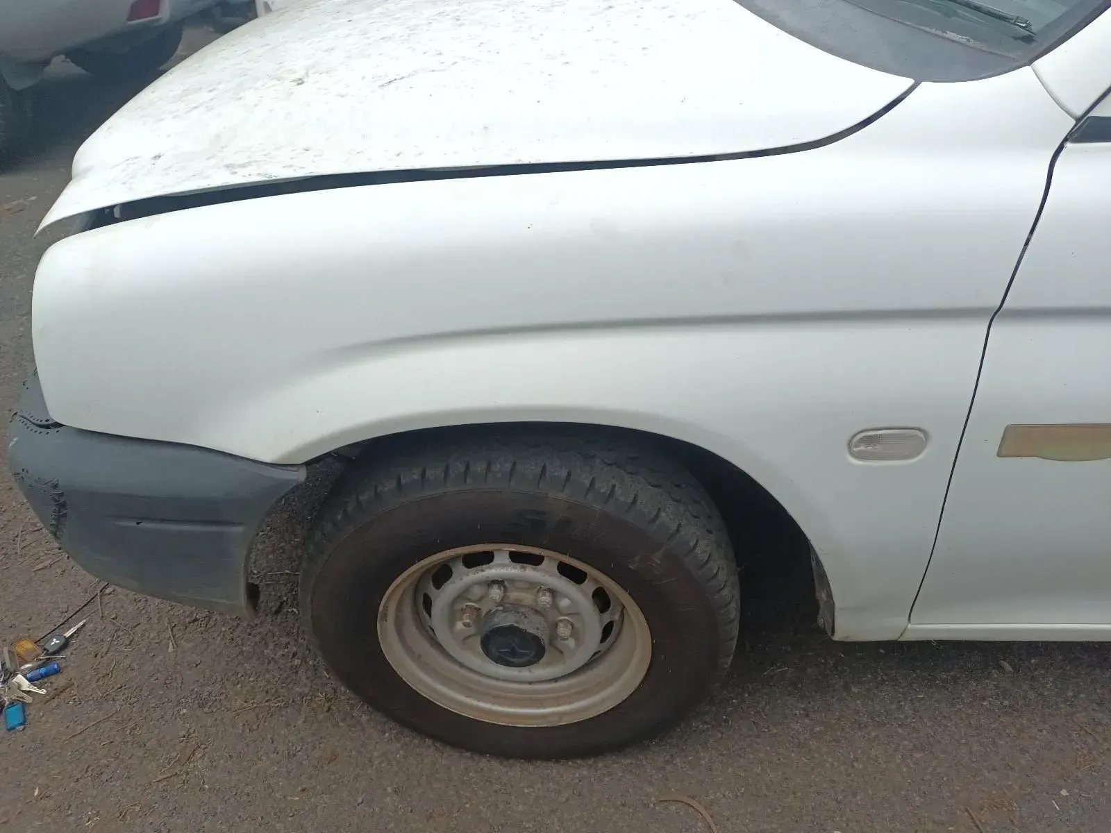 White Car Front Quarter Panel With Tyre, Missing Hood, on Gray Asphalt — South West 4WD Wreckers In Brisbane, QLD