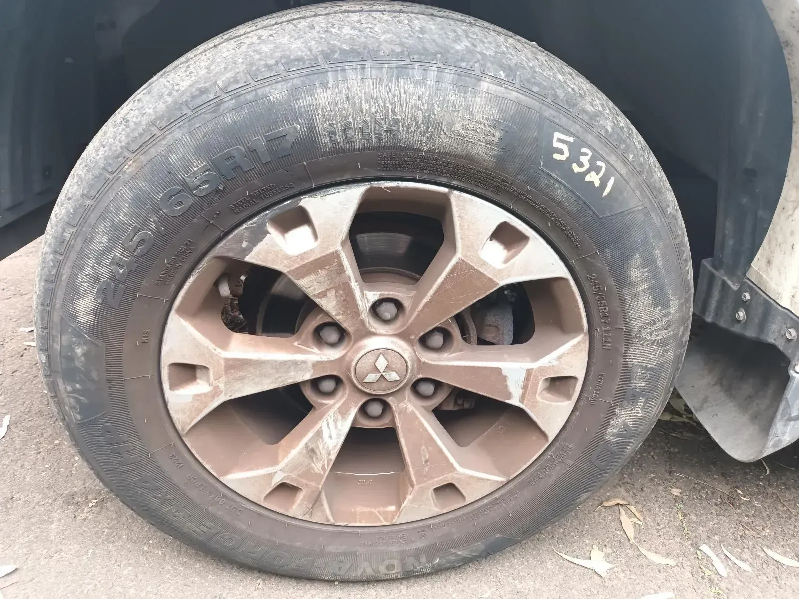 A Dirty Mitsubishi Car Tyre and Rim, Showing the Hubcap and Markings, Outdoors — South West 4WD Wreckers In Brisbane, QLD