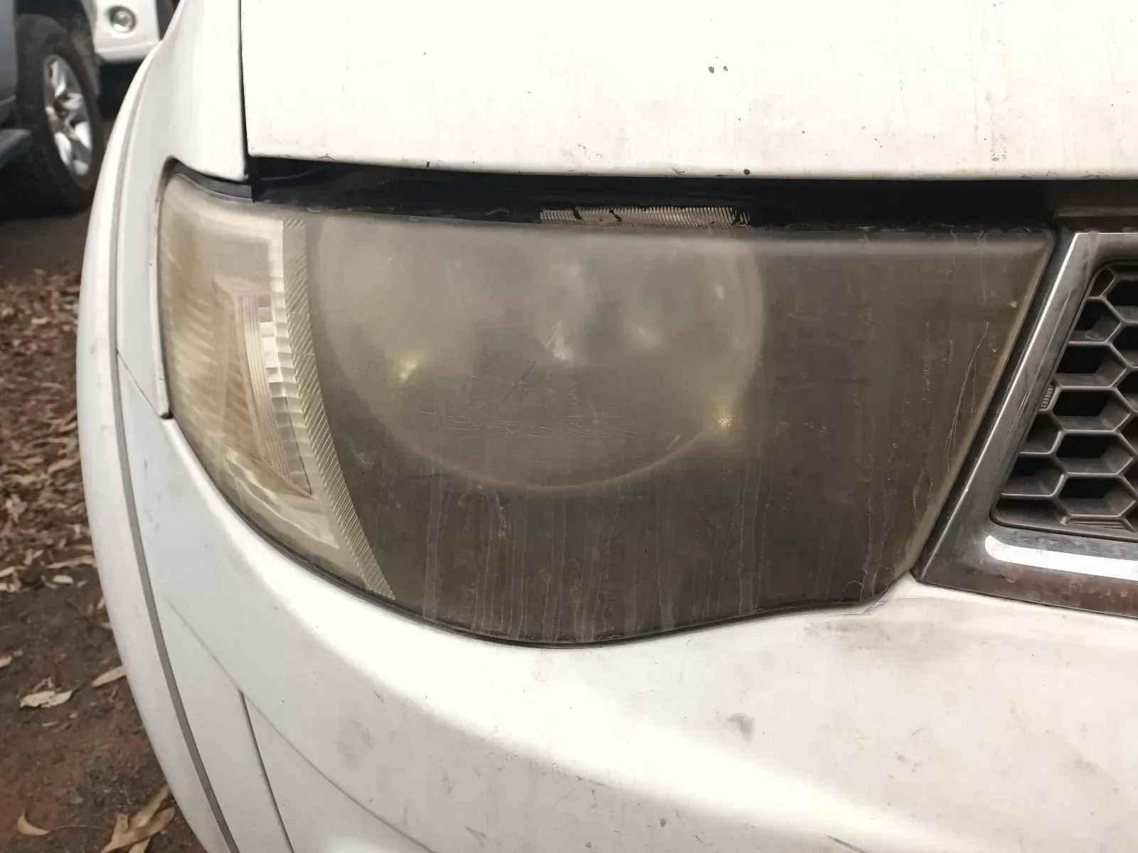 A Dirty, Clouded Car Headlight on a White Car, Covered in Dust and Grime — South West 4WD Wreckers In Brisbane, QLD