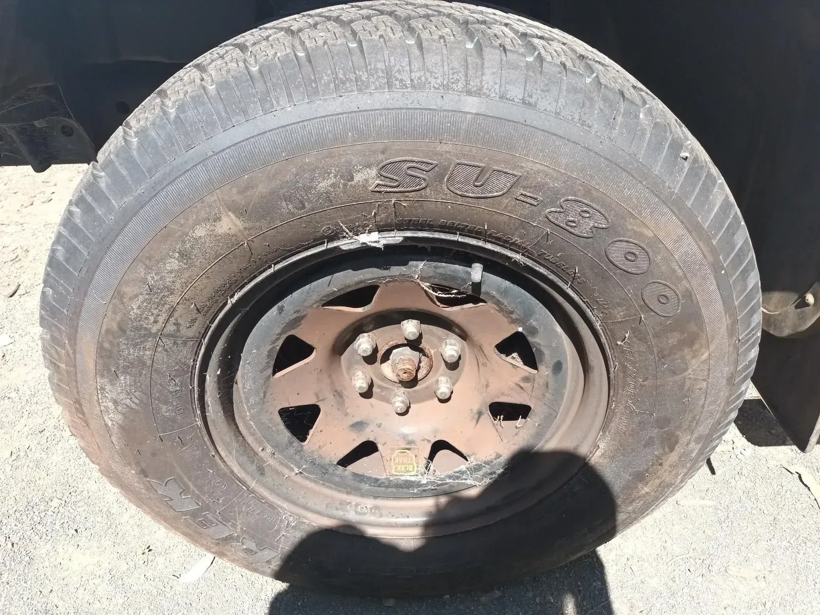 Dirty, Worn Tyre on a Rusty, Dark Metal Wheel. Shadow Visible Below — South West 4WD Wreckers In Brisbane, QLD