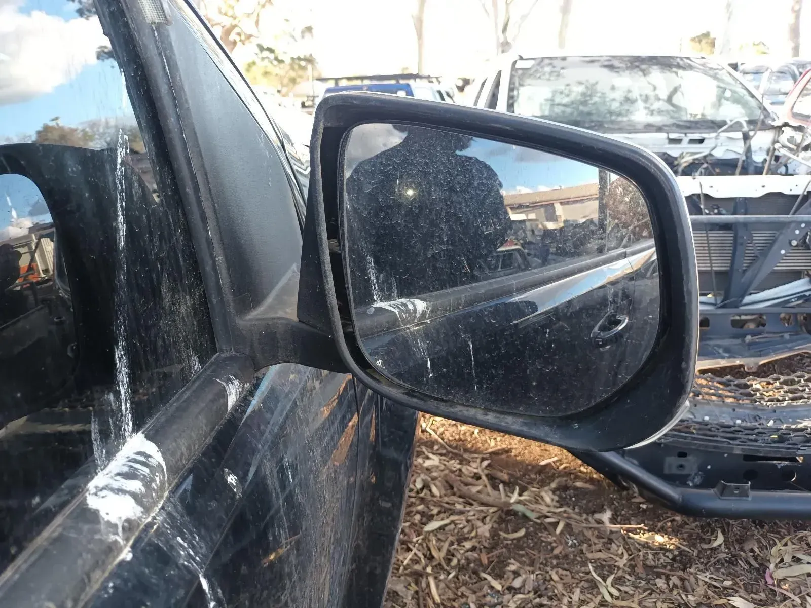 Black Side Mirror of a Car Reflects a Person and Debris in a Junkyard — South West 4WD Wreckers In Brisbane, QLD