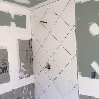 Bathroom wall with white tiles in a diamond pattern, marked with black lines. Wall in progress.