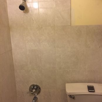 Bathroom with beige tile walls, showerhead, and toilet with a smartphone on the top.